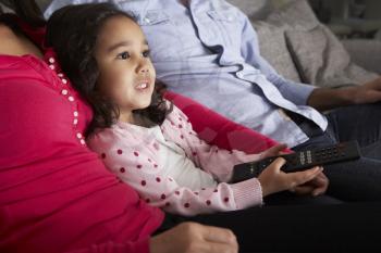 Hispanic Girl Sitting On Sofa And Watching TV With Parents