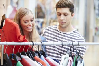 Couple Looking At Clothes On Rail In Shopping Mall