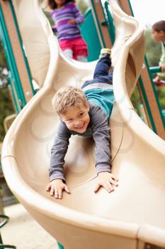Young Boy Playing On Slide In Playground