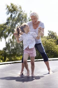 Grandmother And Granddaughter Bouncing On Trampoline