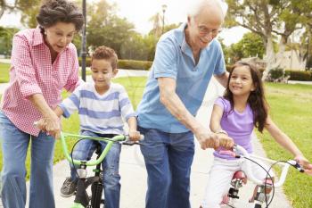 Grandparents Teaching Grandchildren To Ride Bikes In Park