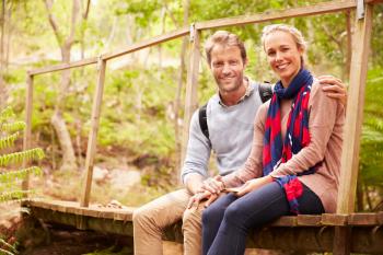 Happy couple sitting on a bridge in a forest, looking to camera