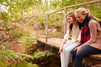 Mother and daughter sitting on bridge in a forest, side view