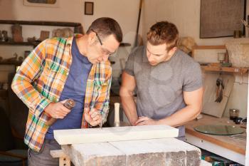 Stone Mason With Apprentice At Work On Carving In Studio