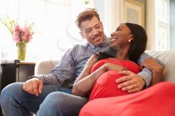 Pregnant Couple At Home Relaxing On Sofa Together
