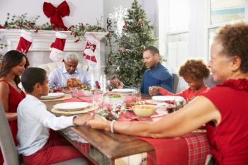 Family With Grandparents Saying Grace Before Christmas Meal