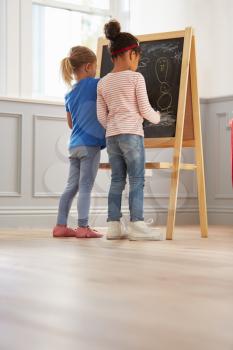 Two Girls Drawing Picture On Blackboard At Home