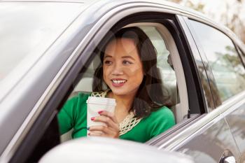 Female Asian driver drinking take-away drink in a car
