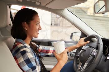 Hispanic female driver holding take away drink, in car view