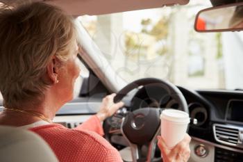 In car view of senior female driver holding take away drink