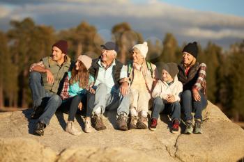 Multi generation family sitting on rocky outcrop near a forest