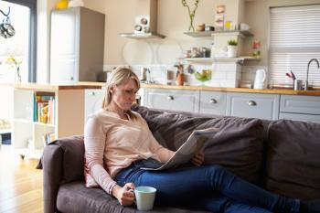 Woman Relaxing On Sofa Reading Newspaper In Modern Apartment