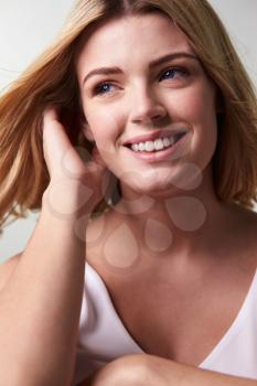 Smiling blonde woman looking away, touching hair, vertical
