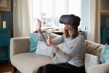 Woman Sits On Sofa At Home Wearing Virtual Reality Headset