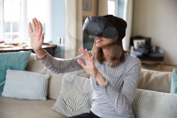 Woman Sits On Sofa At Home Wearing Virtual Reality Headset