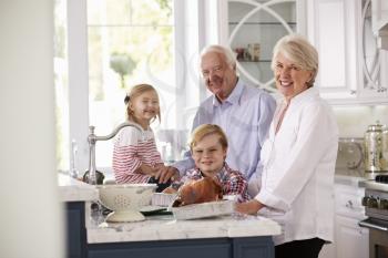 Children And Grandparents Make Roast Turkey Meal In Kitchen