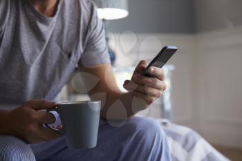 Man Wearing Pajamas Using Mobile Phone In Bedroom