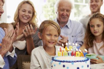 Boy Blows Out Birthday Cake Candles At Family Party