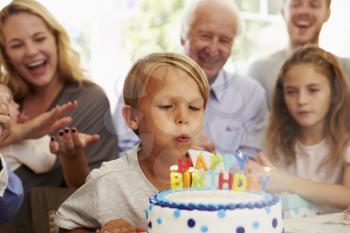 Boy Blows Out Birthday Cake Candles At Family Party