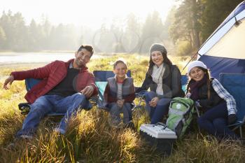 Happy family on a camping trip sit by tent looking to camera