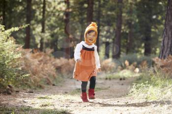 Asian toddler girl walking alone in a forest, front view