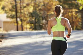 Caucasian woman jogging on country road, back view close up
