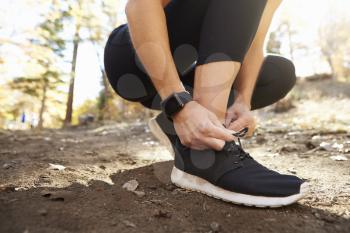Woman ties sports shoe before run in forest, close up detail