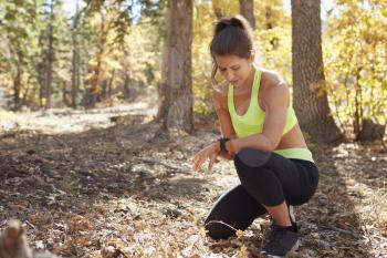Female runner kneels in forest looking at smartwatch