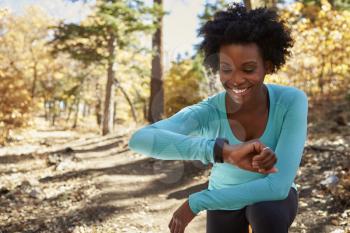 Young black woman in a forest checking smartwatch and smiling