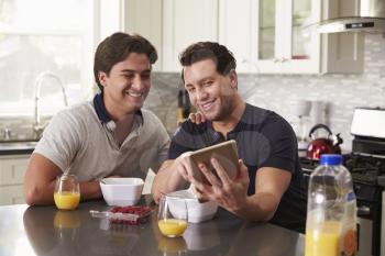 Male gay couple looking at tablet computer over breakfast