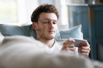 Man Relaxing On Sofa Checking Mobile Phone