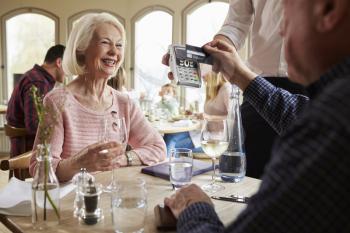 Senior Couple With Waiter Paying Bill In Restaurant