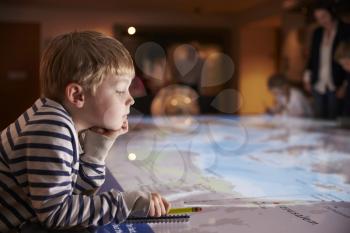 Boy On Trip To Museum Looking At Map And Writing In Notebook