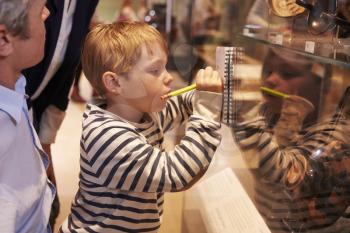 Family Looking At Artifacts In Glass Case On Trip To Museum