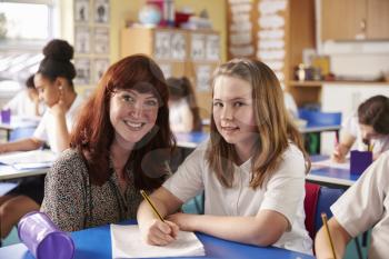 Primary school teacher with girl at her desk look to camera