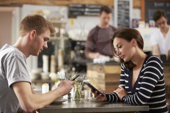 Adult couple sitting in a cafe using smartphones, close up
