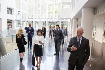 Businesspeople Using Technology In Busy Lobby Area Of Office