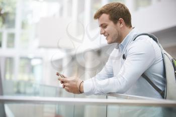 Adult male student using smartphone in university interior
