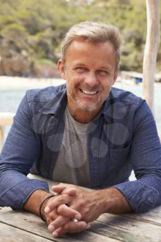 Middle aged Caucasian man at a table by the sea, vertical