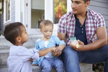 Father Giving Children Candy On Steps Outside Hose