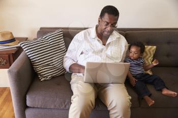 Grandfather And Grandson Sit On Sofa At Home Using Laptop