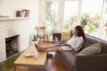 Woman Relaxing On Sofa At Home Using Laptop