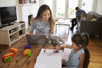 Mother Uses Laptop Whilst Father Plays With Children At Home