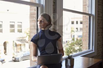 Businesswoman Sitting By Window Working On Laptop