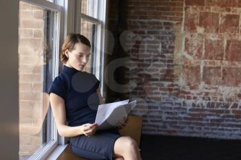 Businesswoman Sitting By Window Reading Documents