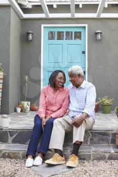 Senior couple sit on steps outside their house, vertical