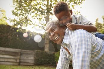 Young black boy climbing on his grandfathers back in garden