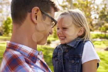 Dad and young daughter pulling faces at each other in a park