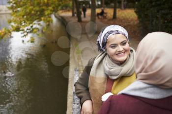 British Muslim Female Friends Talking By River In City