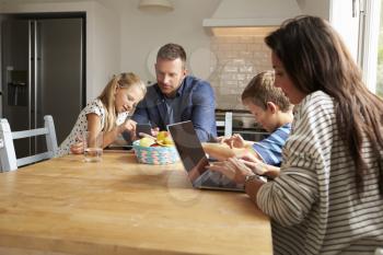 Family Using Digital Devices At Kitchen Table